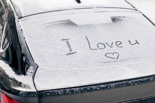 Snow-covered rear window of a car with inscription I love you on it.