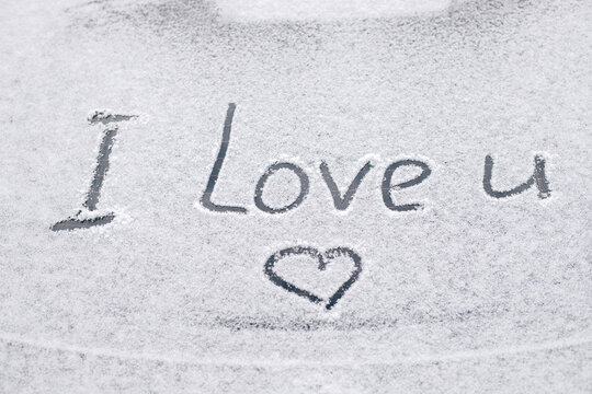 Snow-covered rear window of a car with inscription I love you on it.