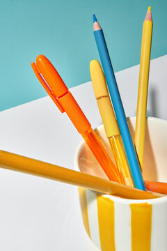 Bright Colored Writing Tools in a Striped Cup on a White Surface