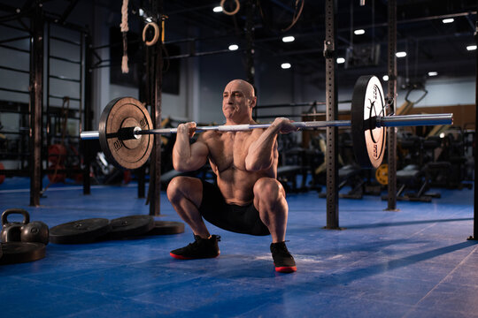 Concentrated aged man squatting with heavy barbell
