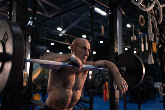 Shirtless aged male athlete leaning on barbell