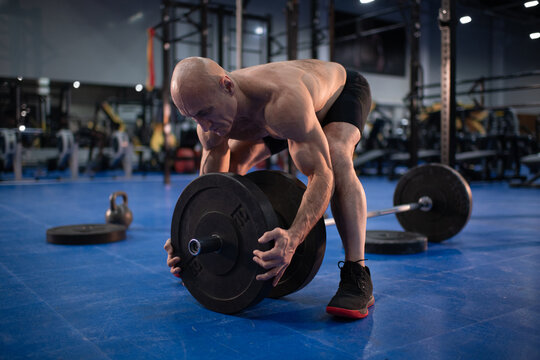 Bald elderly sportsman preparing barbell for training