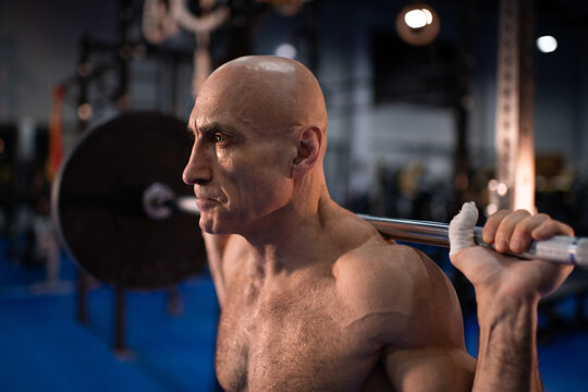 Serious elderly sportsman exercising with barbell