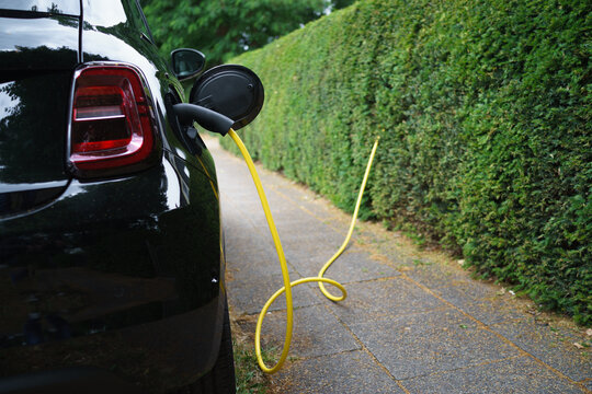 Electric car charging near hedge on a sidewalk