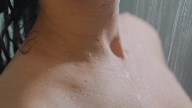 Reflective hotel shower neck and shoulder closeup, droplets tracing collarbone and wet hair, soft morning light and steam in boutique bathroom, solo guest pausing in calm private moment