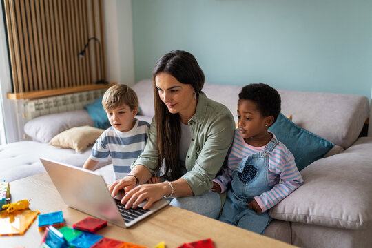 Mother homeschooling diverse children using laptop at home