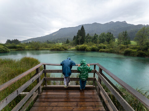 Children Look at Water From Wooden Platform in Rainy Weather