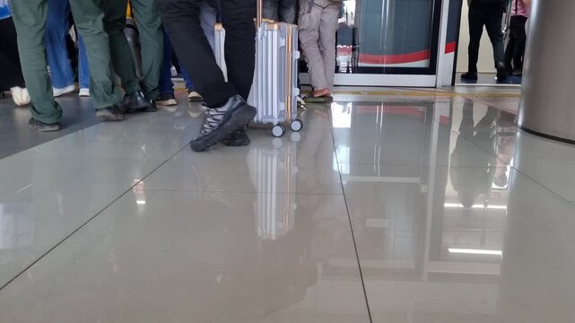 Commuters walking through automatic doors at a busy transit station reflected on shiny tiles.