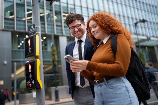 Business colleagues checking smartphone at city crosswalk