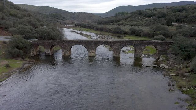 Aerial view of Puente de Piedra in Coria, C&aacute;ceres, Spain. Historic multi-arch stone bridge over Alag&oacute;n River surrounded by rural landscape and flowing water. 