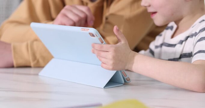 Father and his son using tablet at white table indoors, closeup