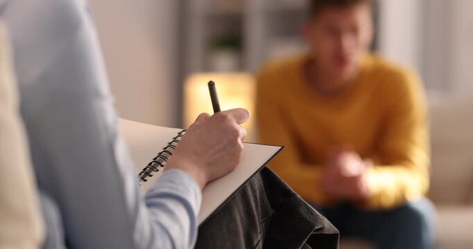 Professional psychologist making notes during therapy session with patient indoors, selective focus