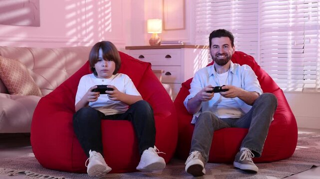 Emotional father and son with controllers playing video game on poufs at home