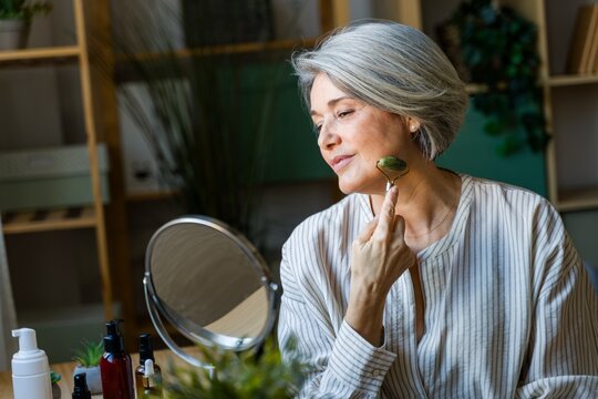 Woman Using Face Roller At Mirror