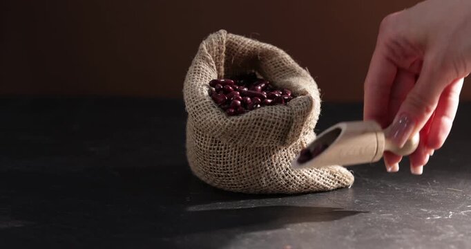 Woman taking dried red beans from burlap bag at black table, closeup