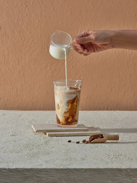 Pouring Milk into Iced Coffee Against Minimalistic Beige Background