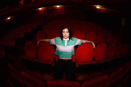 Woman sits alone in red theater seats during a performance