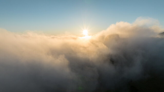 Aerial view of the sun rising over a thick sea of clouds with mountain peaks peeking through the mist in Madeira, Portugal.