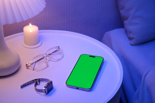 Nightstand essentials with smartphone, eyeglasses, watch and candle