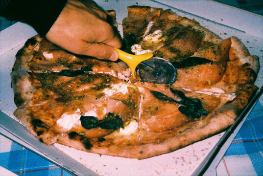 a man cuts a salmon pizza with a yellow pizza cutter, 35mm film