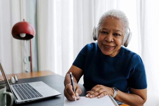 Older woman in headphones writing notes at home