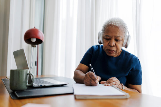 Senior woman with grey hair writing notes at home