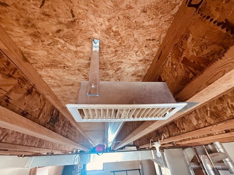 Ceiling air vent register connected to HVAC ductwork in unfinished basement with exposed wooden joists and residential construction framing
