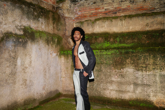 A Person Poses in a Worn-Down Space With Brick Walls and Green Moss
