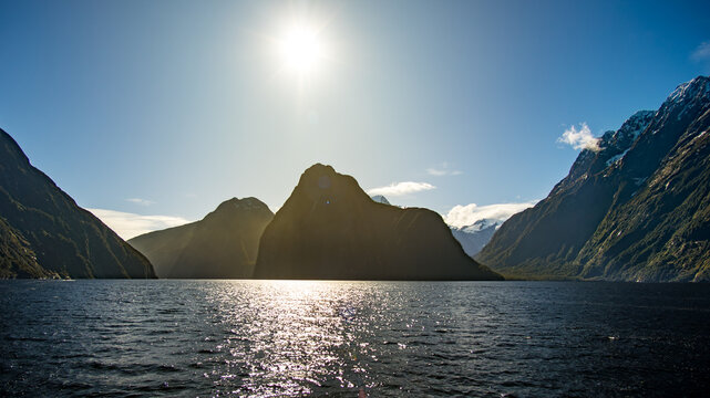 Silhouettes des pics de Milford Sound en contre-jour avec soleil &eacute;blouissant et reflets dor&eacute;s sur l'eau, Fiordland, &icirc;le du Sud, Nouvelle-Z&eacute;lande