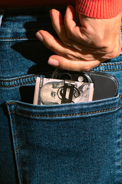 Hand Putting Cash and Smartphone into Blue Jeans Back Pocket
