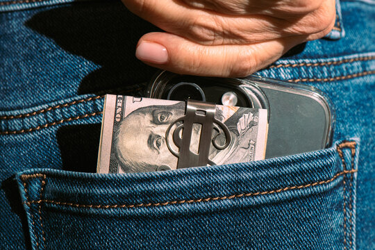 Hand Putting Cash and Smartphone into Blue Jeans Back Pocket