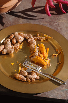 Fresh Turmeric Root on a Golden Plate With a Peeler