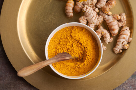 Ground Turmeric and Fresh Roots Placed on a Metal Tray