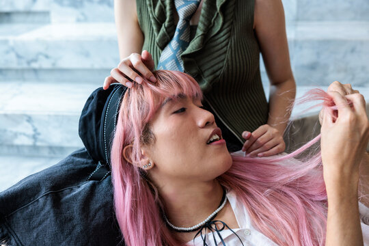 Pink-haired person relaxes while another person plays with their hair