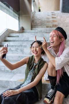 Friends laugh and take selfie on marble stairs.