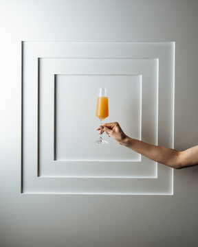 Hand holding orange cocktail in flute glass against white wall