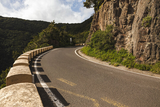 Winding forest road with stone barrier along a rocky hillside.