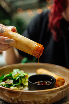 Spring roll dipped in sauce above salad bowl 