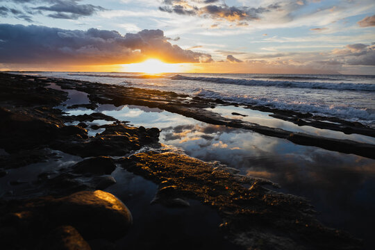 Golden sunset over ocean waves and rocky coastline.
