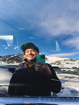 Man taking phone selfie reflected in car window