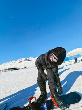 Kid fastening snowboard bindings on snowy slope