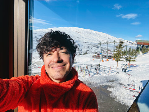 Man taking selfie near window overlooking snowy ski mountains