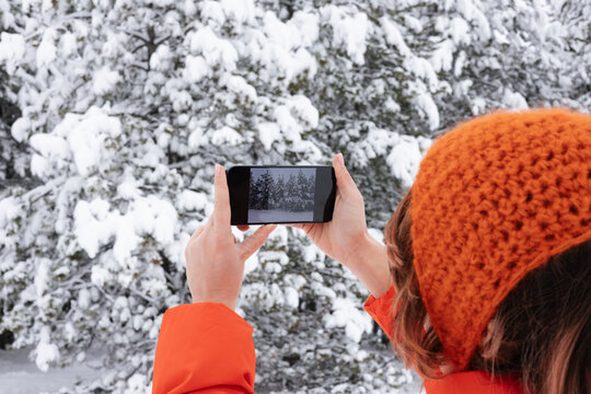 Woman In Orange Jacket Taking a Picture of Snowy Trees On Her Phone 
