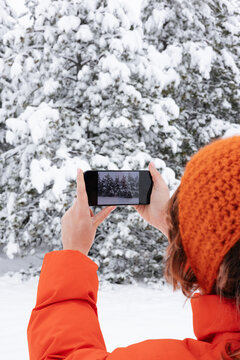 Woman In Orange Jacket Taking a Picture of Snowy Trees On Her Phone 