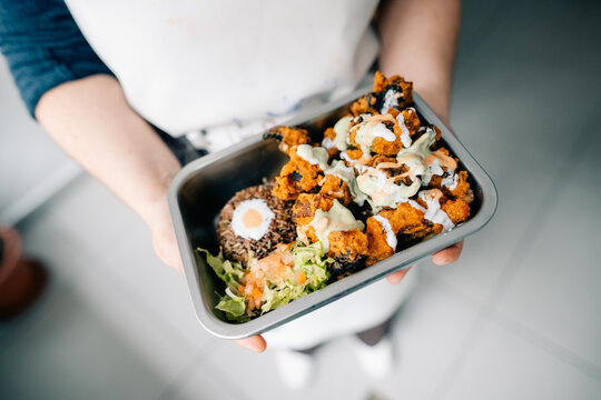 Person Holds a Meal With Chicken, Lettuce, and Sauce in a Kitchen