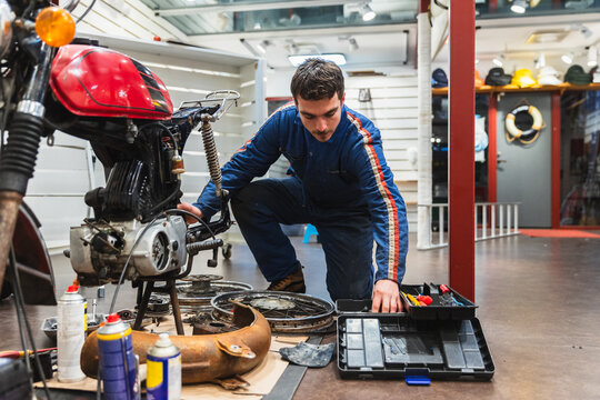 Young Mechanic Working on Red Vintage Motorbike Restoration