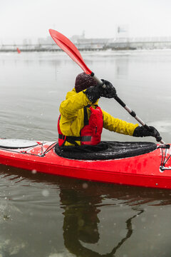 Side View of Kayaker Paddling Red Boat in Icy Urban Bay