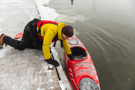 Man Launching Red Kayak into Icy Ocean Water from Concrete Pier