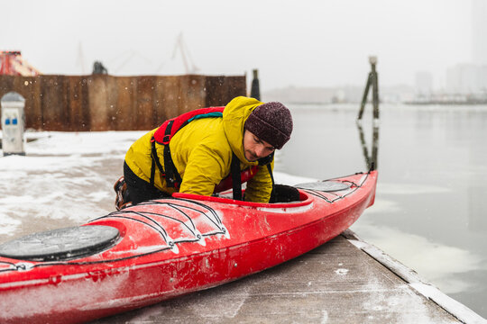 Man Launching Red Kayak into Icy Ocean Water from Concrete Pier