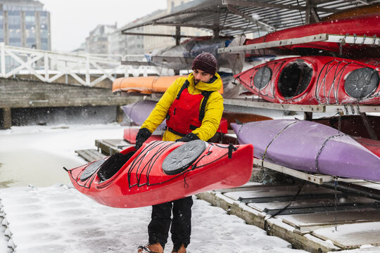 Adventurer Lifting Red Kayak from Storage Rack in Winter Harbor